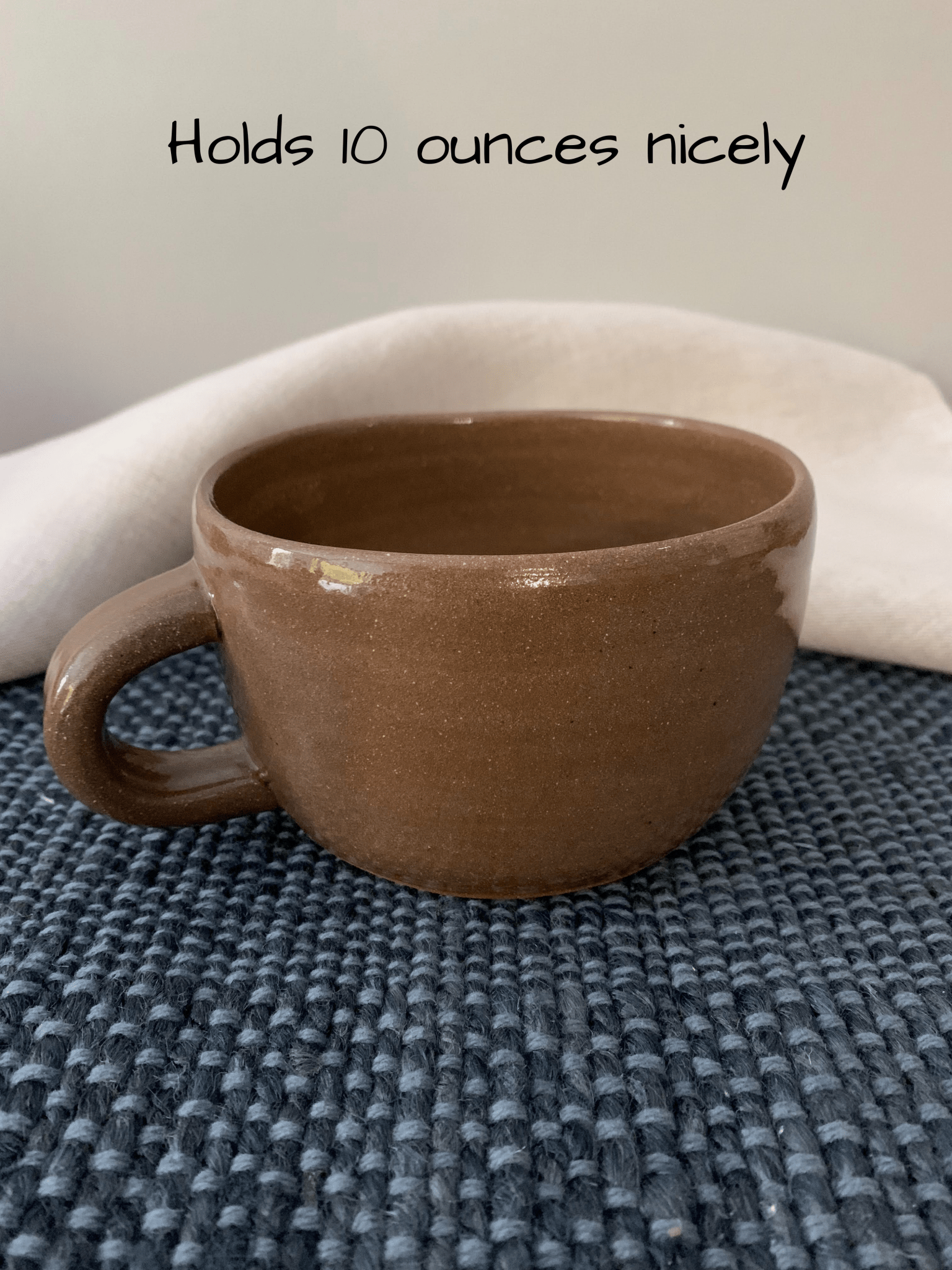 Brown ceramic mug on a textured surface with text indicating capacity.