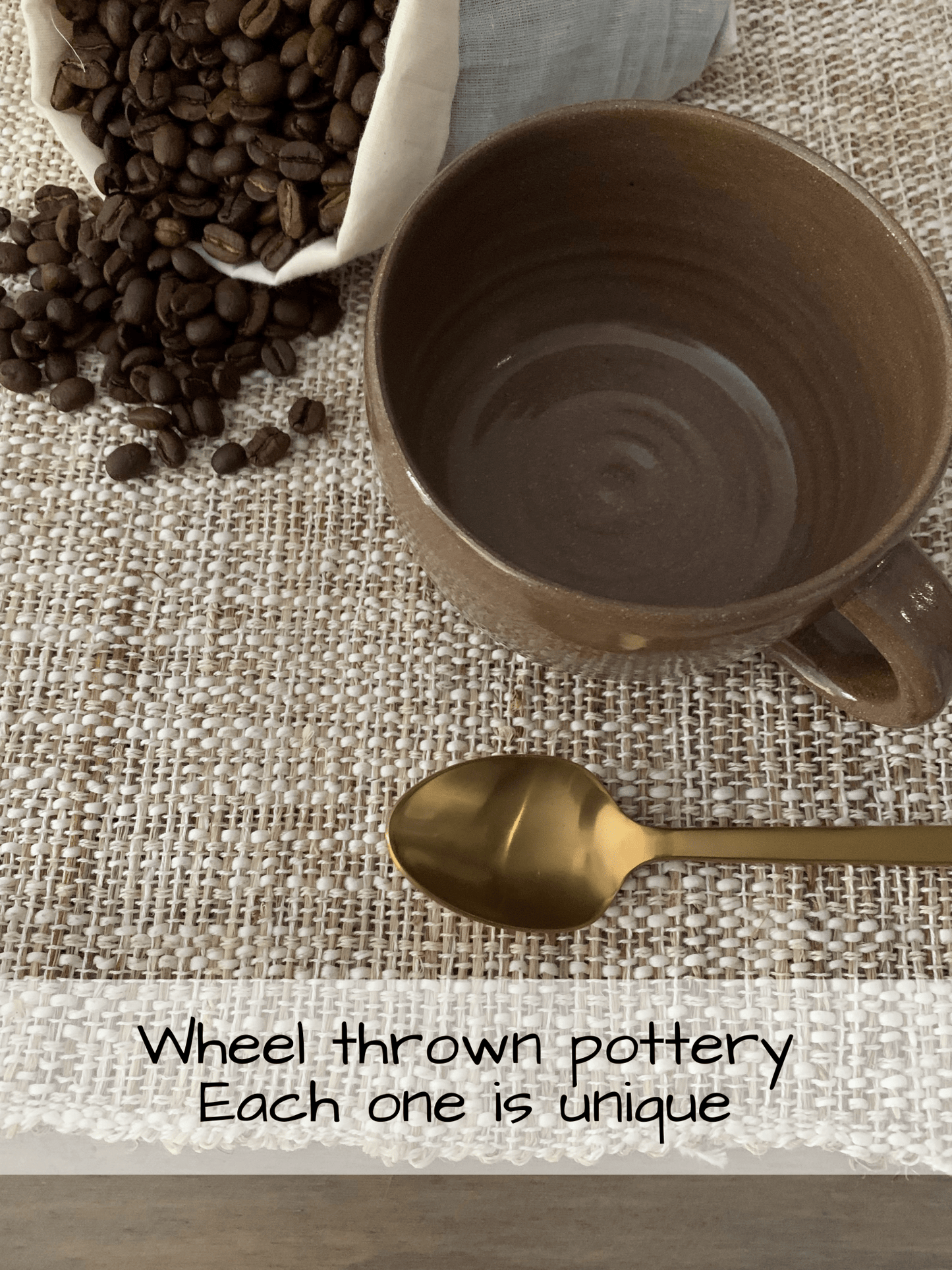 Brown ceramic mug with gold spoon and coffee beans on a textured surface
