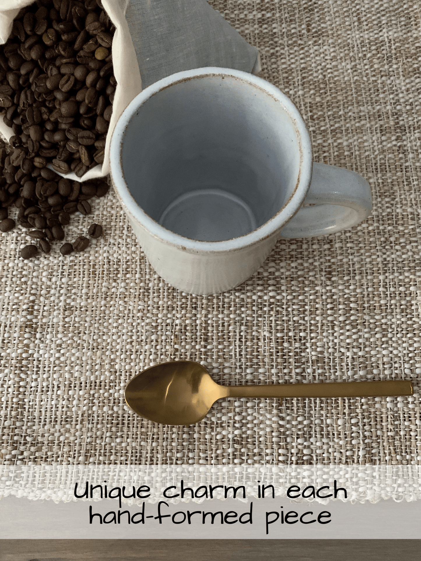white ceramic mug with bag of coffee beans and a gold spoon on a textured place mat on table
