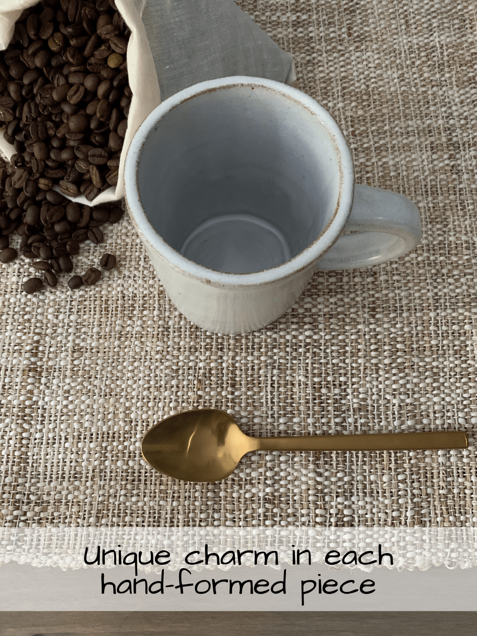 white ceramic mug with bag of coffee beans and a gold spoon on a textured place mat on table