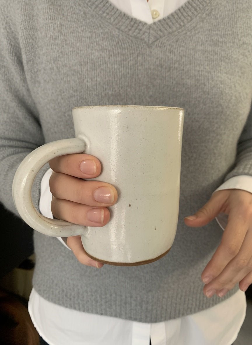 torso of a woman with a closeup on a white pottery mug in her hand