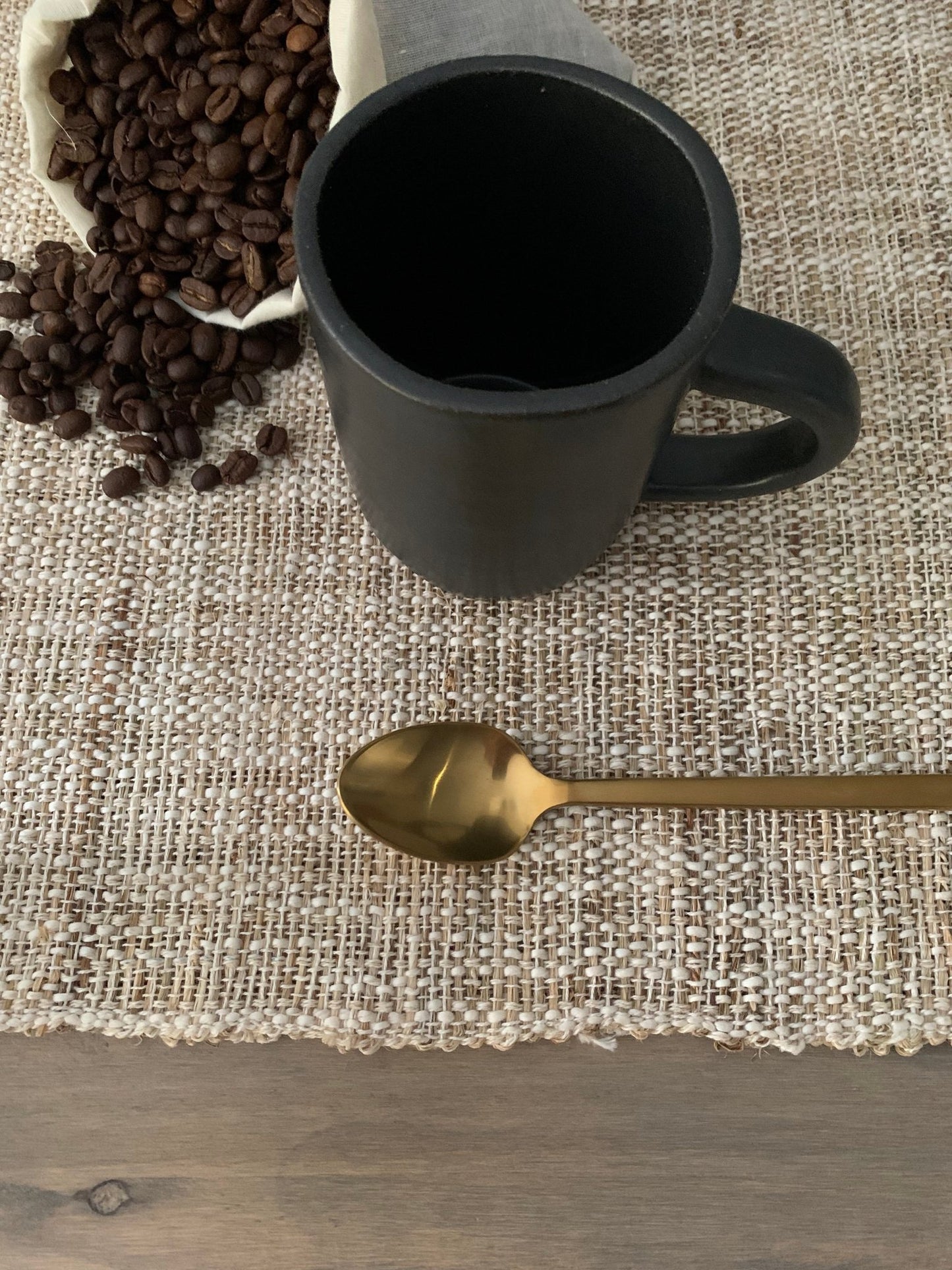 Black stoneware mug with coffee beans and a gold spoon on a textured surface