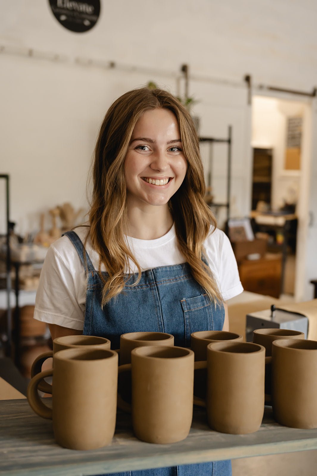 a potter holding a batch of fresh made clay mugs
