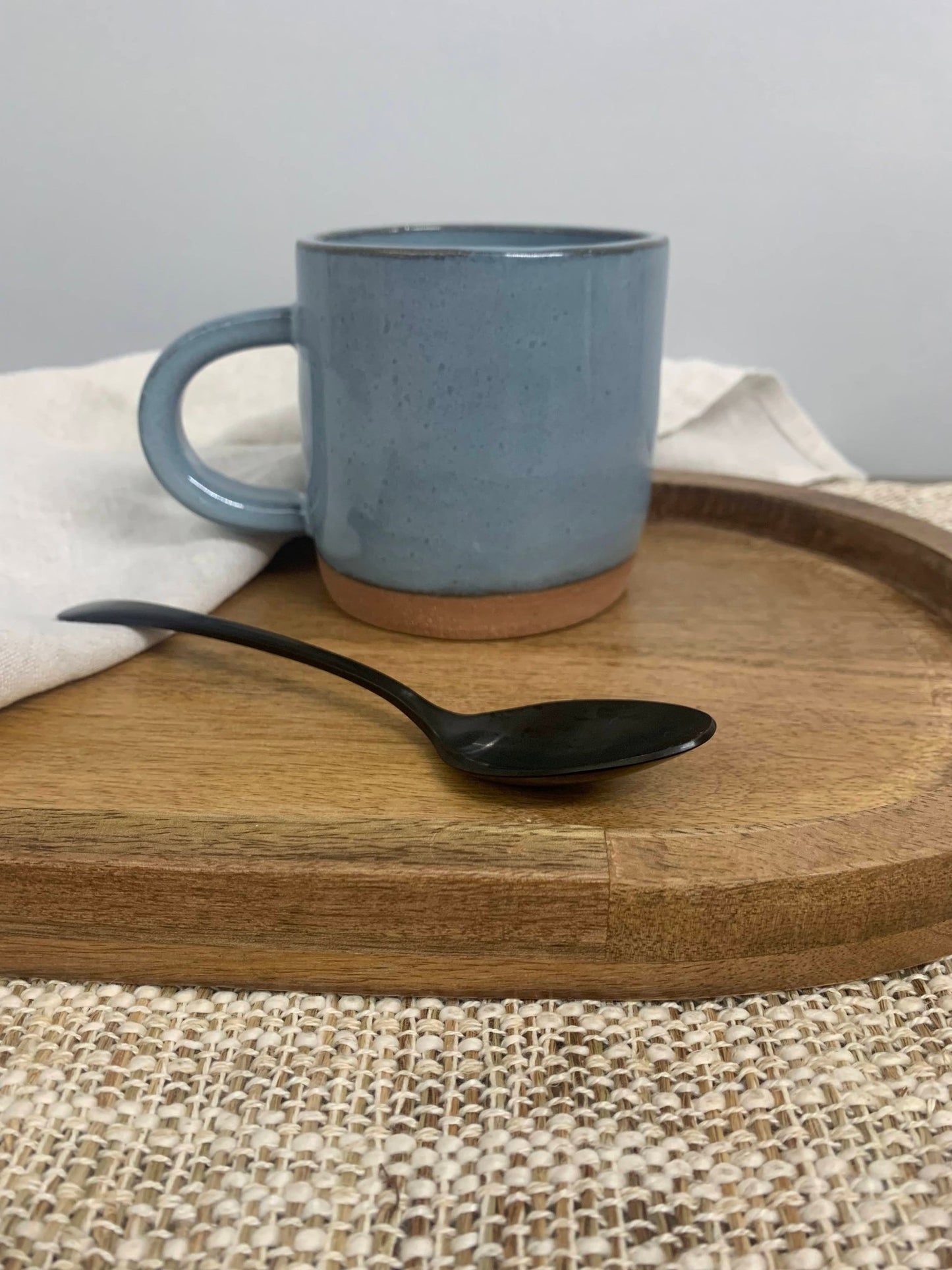 Blue ceramic mug and black spoon on a wooden tray with a neutral background