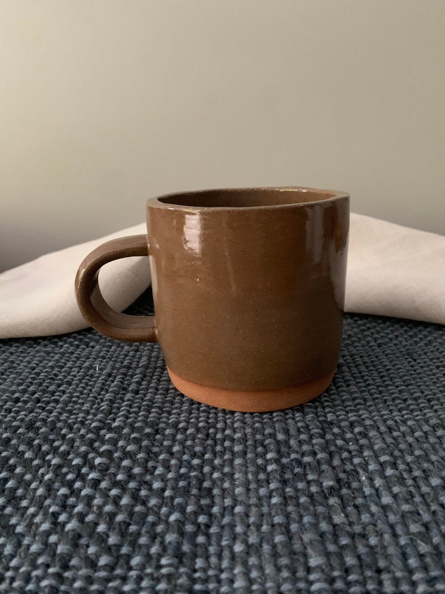 Brown ceramic mug on a textured surface with a neutral background