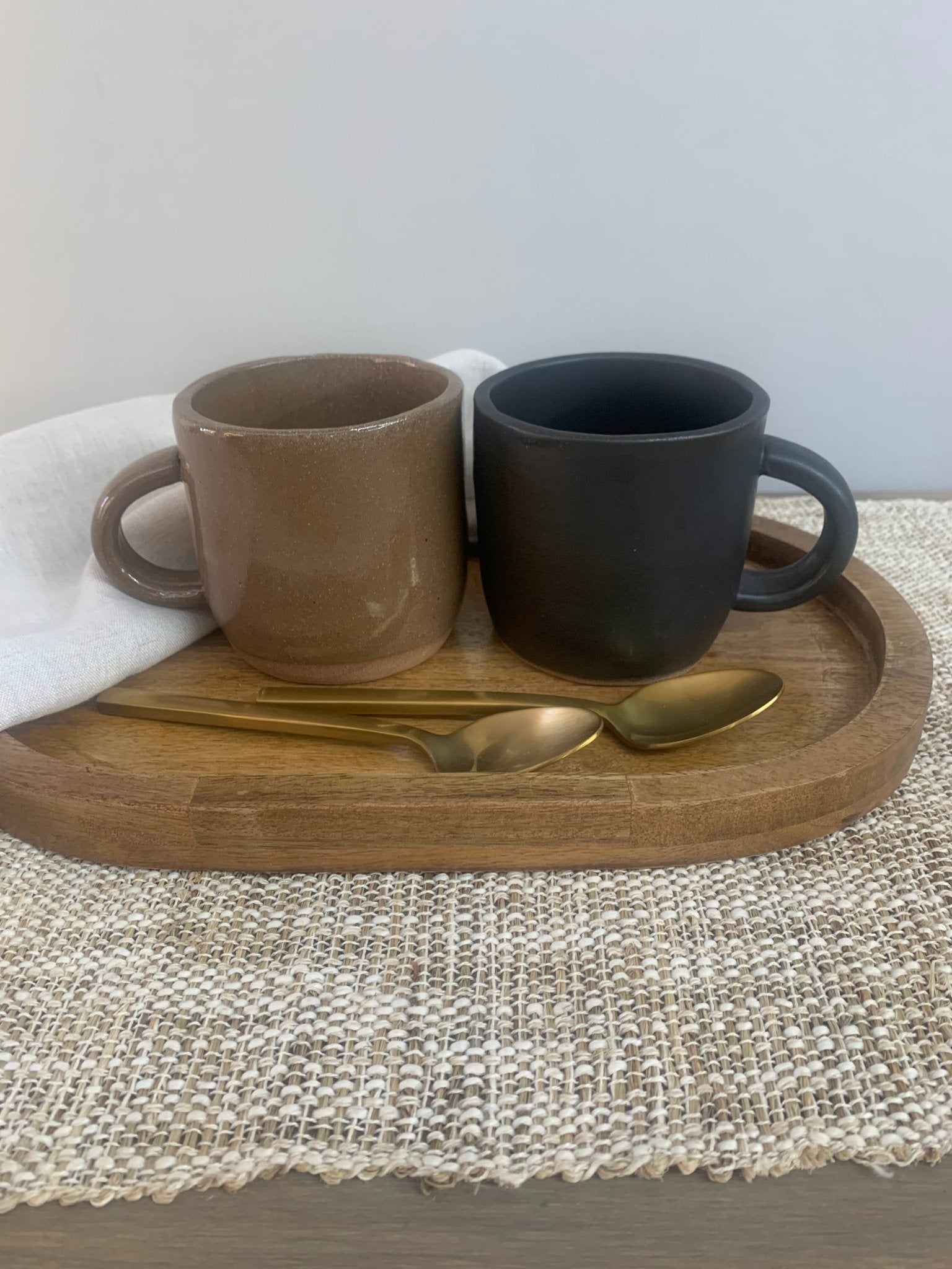 Two ceramic mugs on a wooden tray with gold spoons on a textured surface.