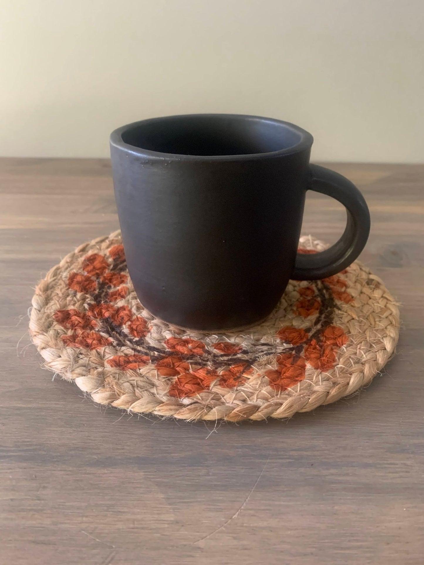 Black ceramic mug on a woven coaster with autumn design on a wooden surface