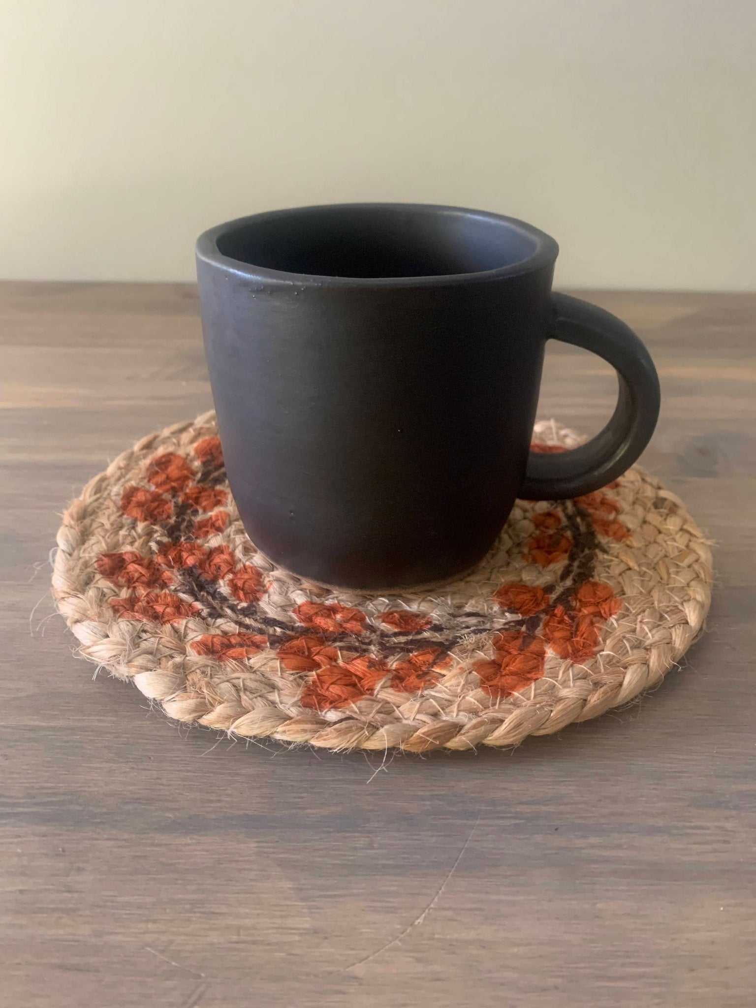 Black ceramic mug on a woven coaster with autumn design on a wooden surface