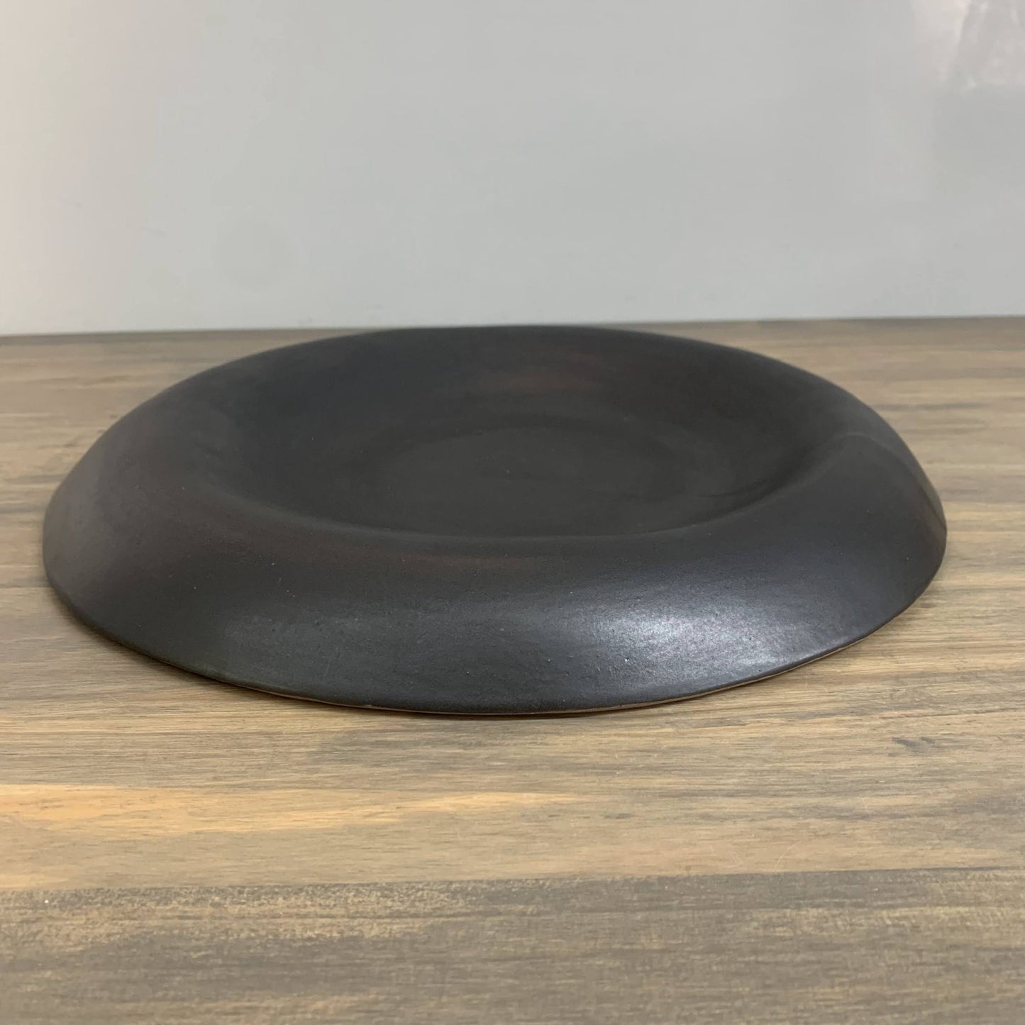 Black handmade ceramic bowl on a wooden surface with a white background