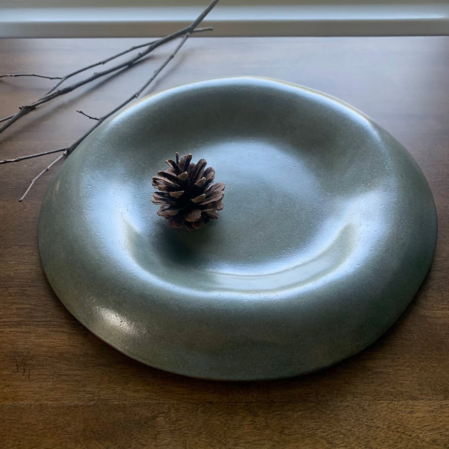Green handmade ceramic plate with a pine cone on a wooden surface