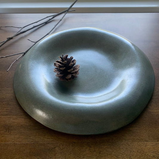 Green handmade ceramic plate with a pine cone on a wooden surface