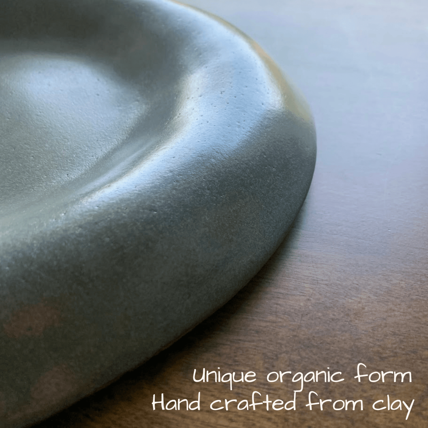 Handcrafted ceramic dish on a wooden surface with text 'Unique organic form Hand crafted from clay'.