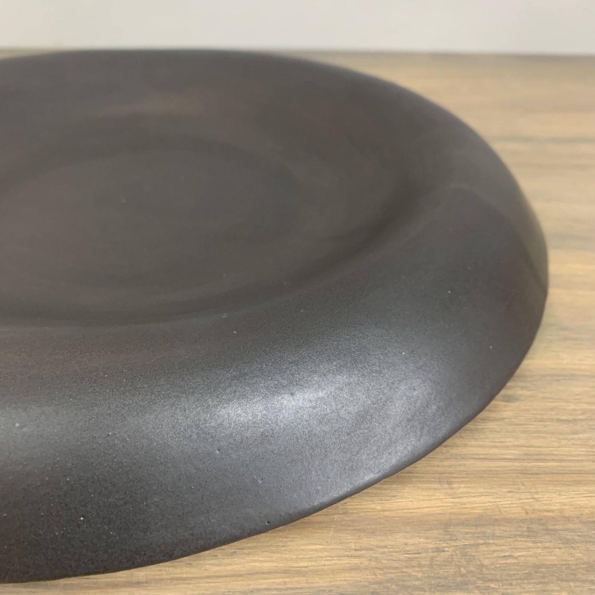 Black ceramic shallow bowl closeup  on a wooden surface