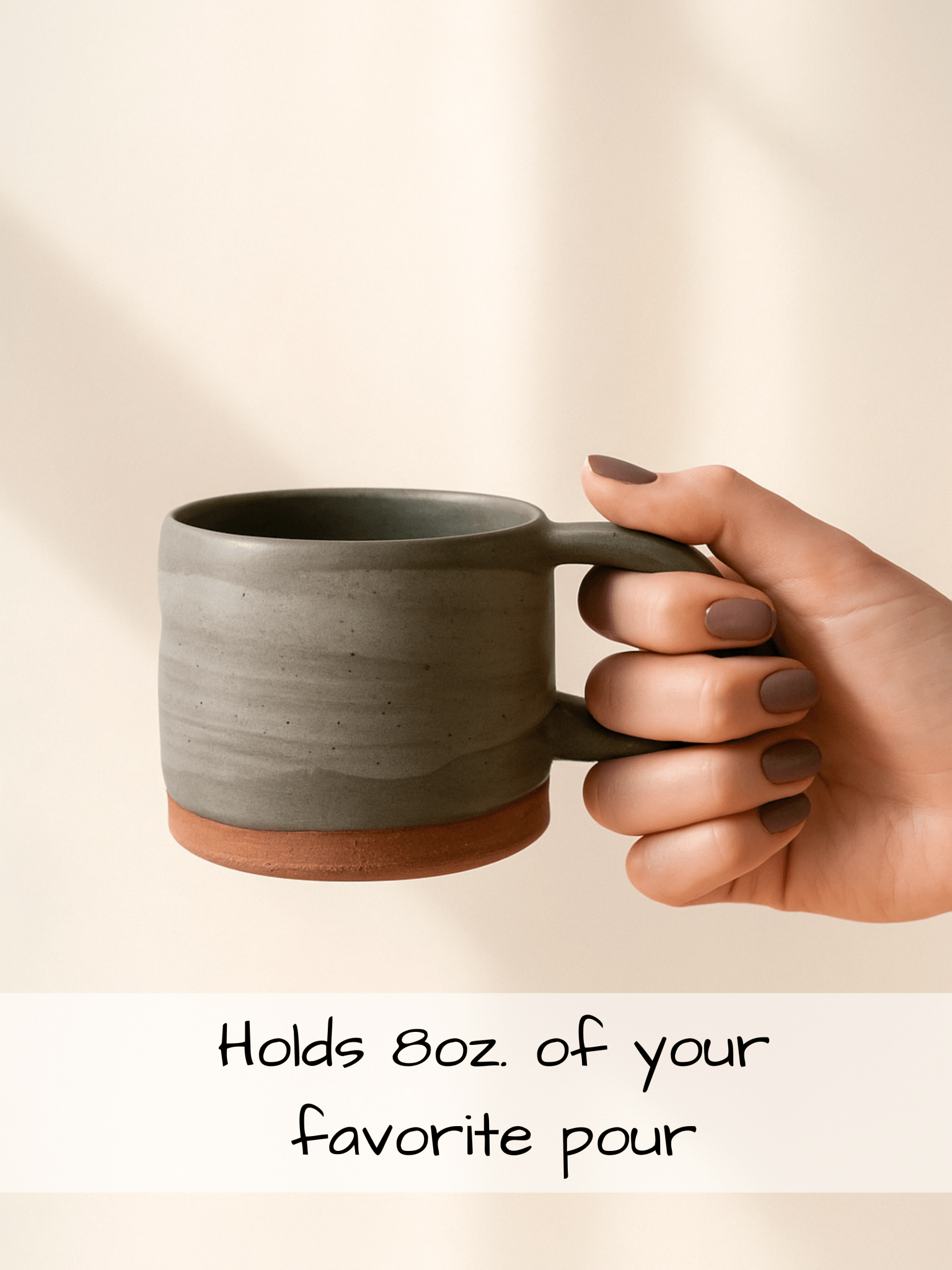 Hand holding a gray ceramic mug with text on a beige background
