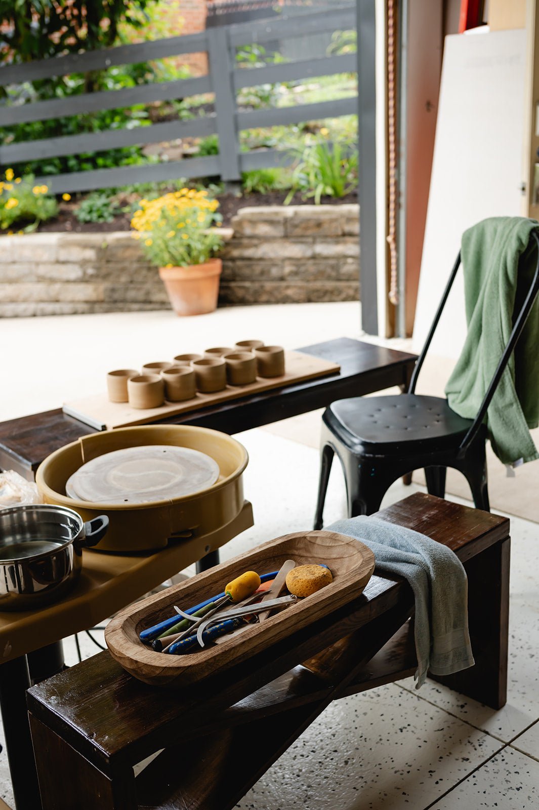Potters' wheel and tools on a table with a garden view outside.