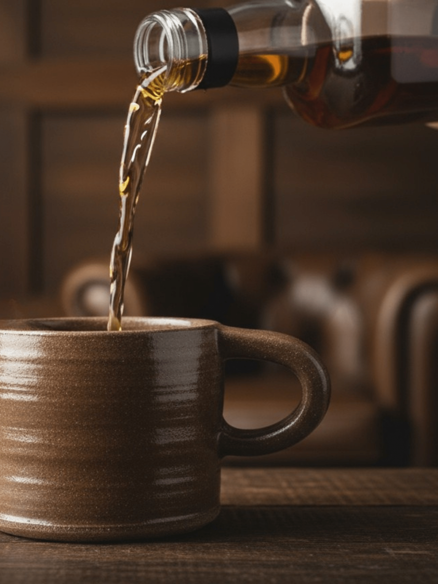 Brown ceramic mug being filled with liquid from a bottle against a blurred background
