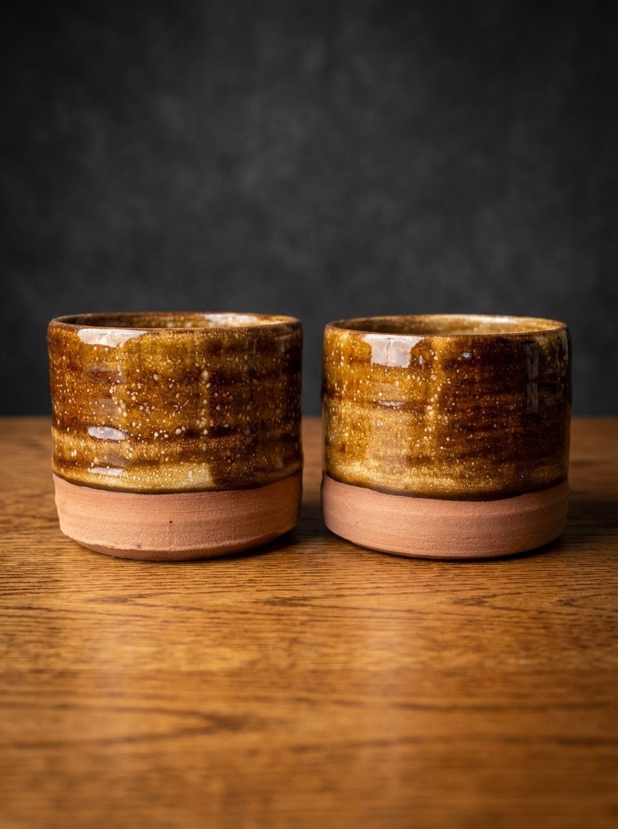 Two brown pottery cups on a wooden surface with a dark background