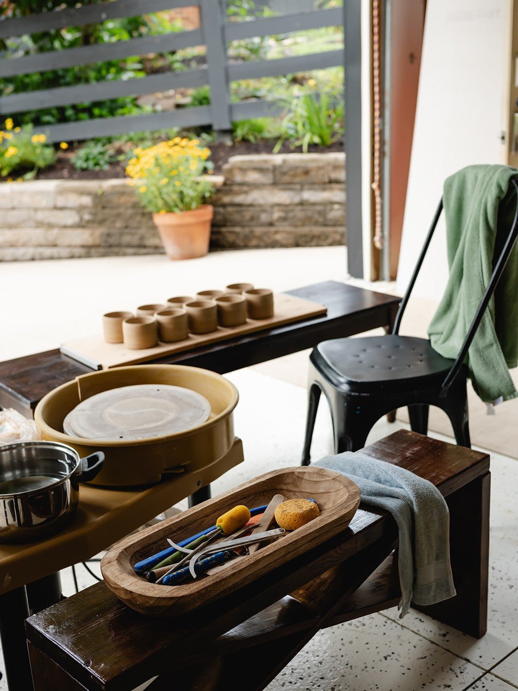 Potters wheel, clay items, and tools on a wooden table with a garden view.