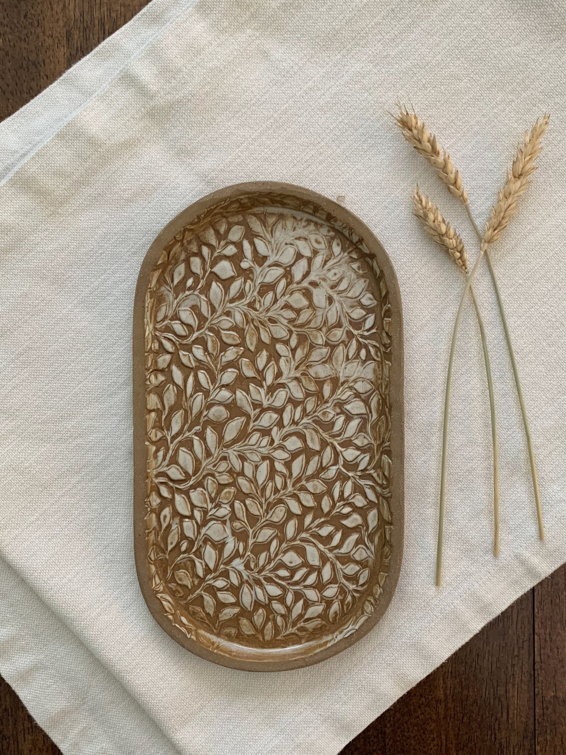 handcrafted Decorative ceramic tray with leaf pattern on a beige cloth with wheat stalks.
