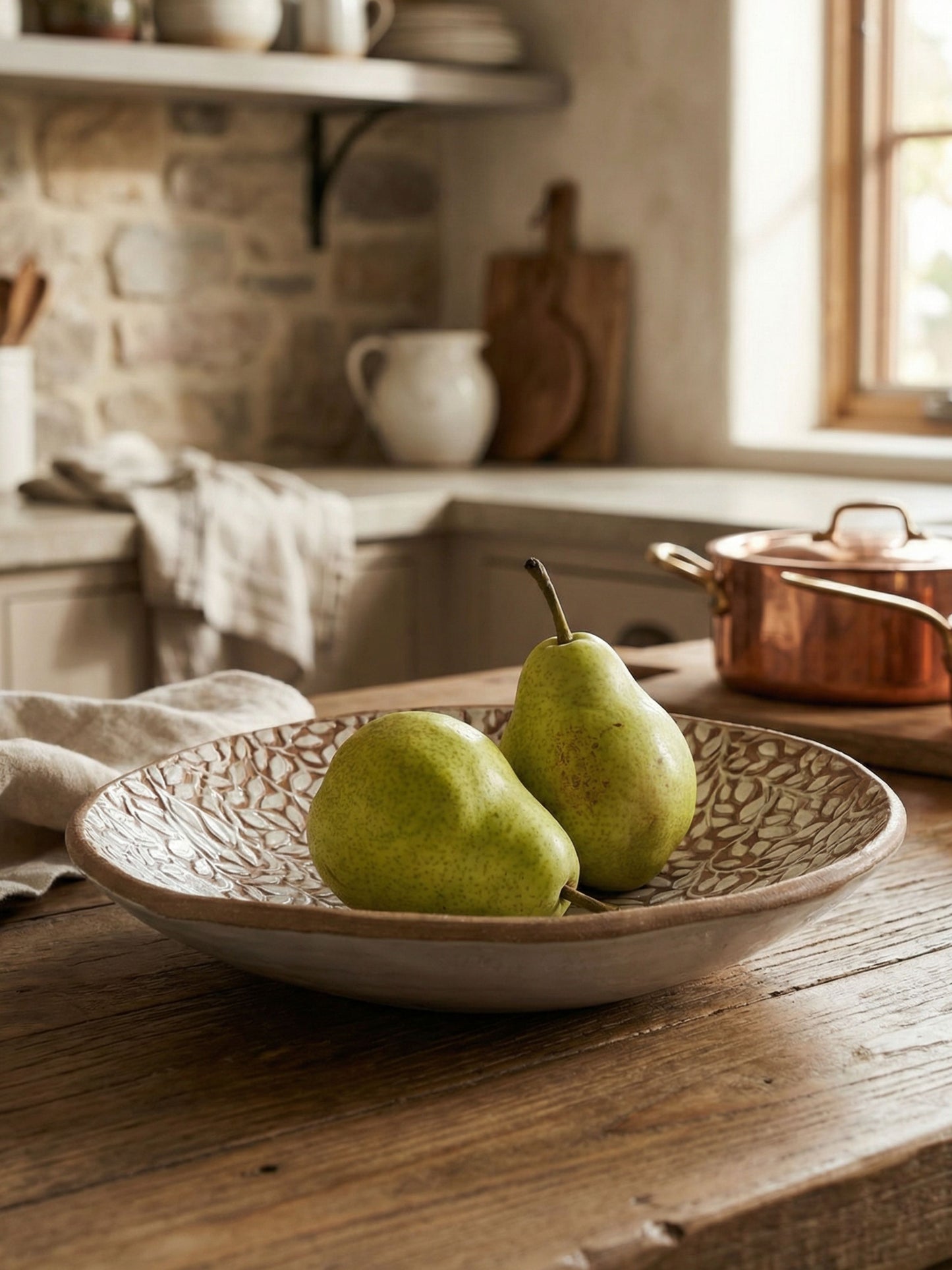 Two pears in a decorative handmade ceramic bowl on a wooden table with a kitchen background.